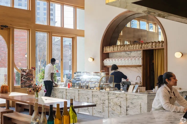 Interior of a restaurant in Atlanta, Georgia, showing a marble service counter, arched architectural details, and floor-to-ceiling windows.