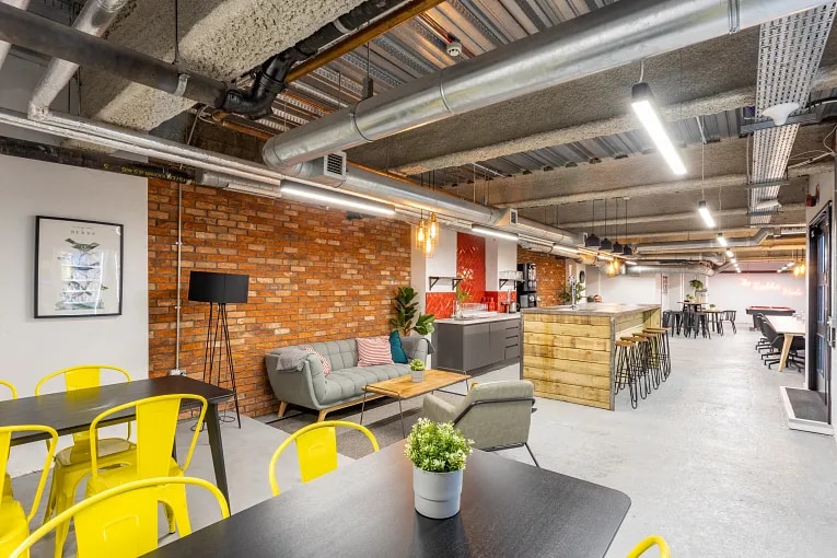 Modern coworking space with open seating, lounge area, exposed ceilings, and a communal kitchen.