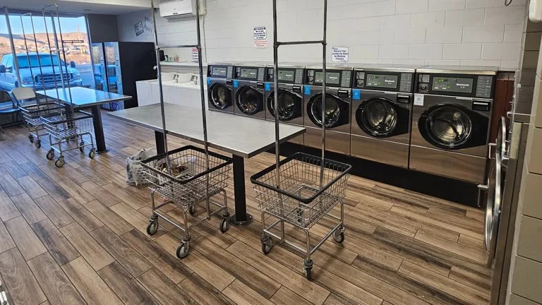 Interior view of a laundromat with wood floors, a row of washing machines and changing tables