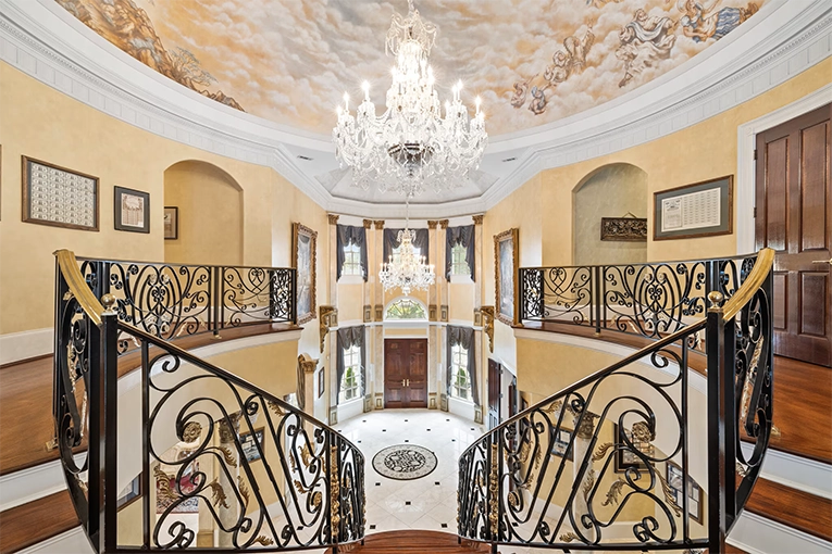 Frescoed ceiling with crystal chandeliers above ornate wrought-iron dual staircase in the Atlanta White House mansion foyer.