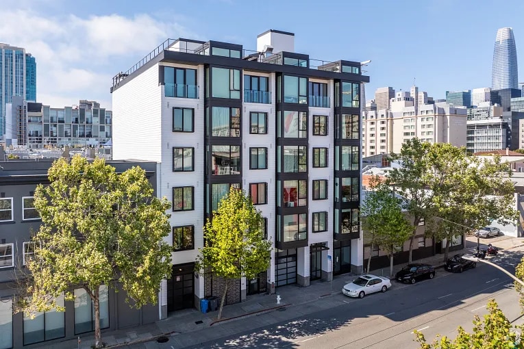 A modern mid-rise multifamily apartment building on a city street in San Francisco, with glass windows, trees, and parked cars in front.