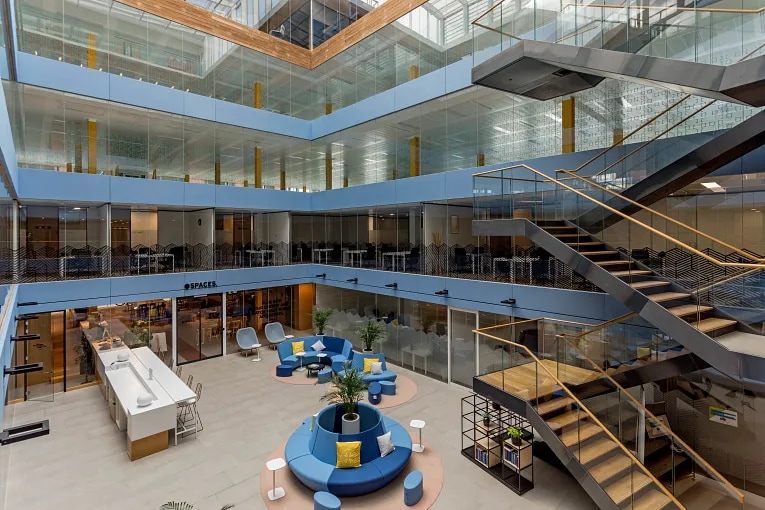 Large modern coworking atrium with open seating areas, glass offices, and central lounge furniture.
