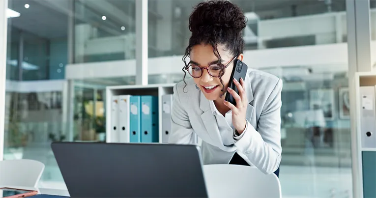 Business professional speaking on the phone while reviewing commercial property listings on a laptop in a modern office.