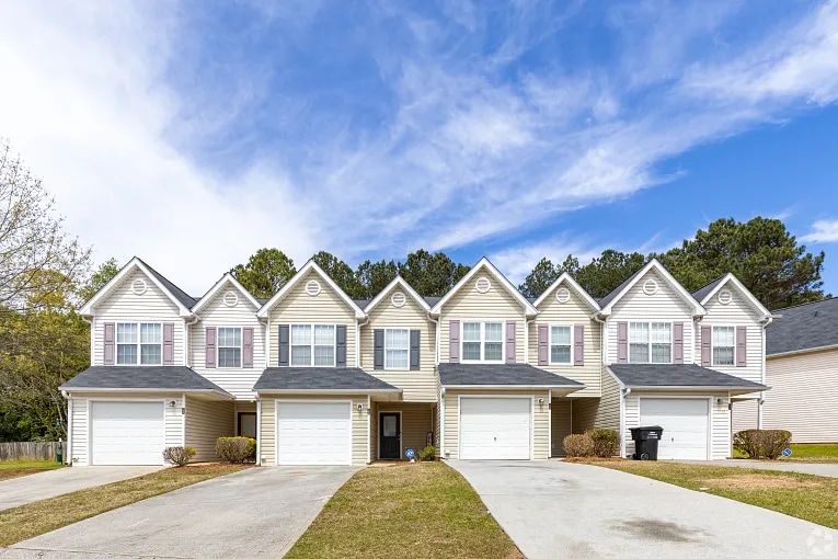 Row of connected two-story townhomes with driveways and garages in a residential neighborhood under a blue sky.
