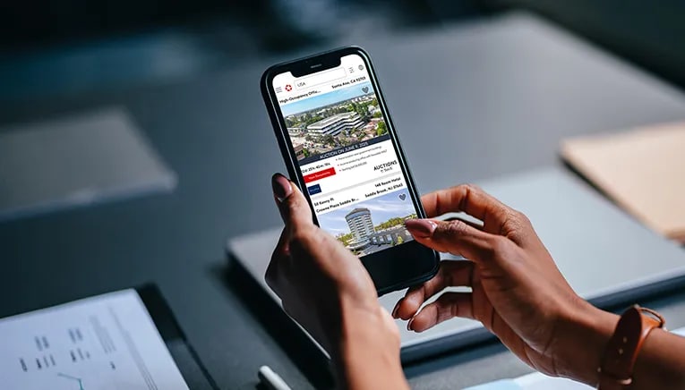Person holding a smartphone displaying commercial real estate auction listings on LoopNet's website.