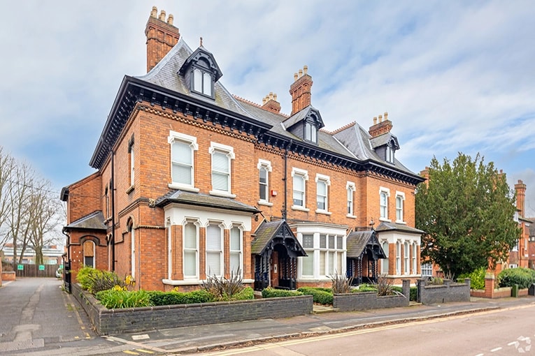 Exterior view of a historic red-brick coworking space in Leicester, UK, featuring Victorian architecture with bay windows and decorative chimneys along a quiet street.