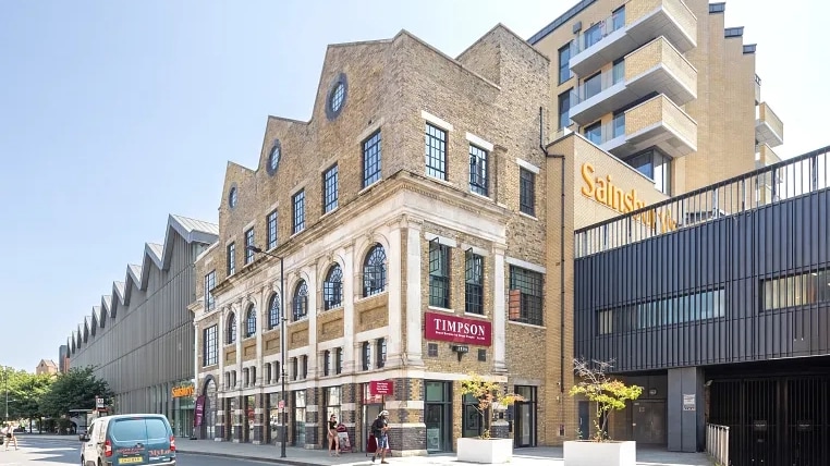 Exterior of a converted brick warehouse with ground-floor retail units and a newer residential block, forming a mixed-use commercial development in London.